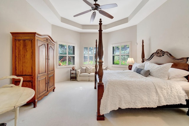 bedroom with ceiling fan, a tray ceiling, and light carpet