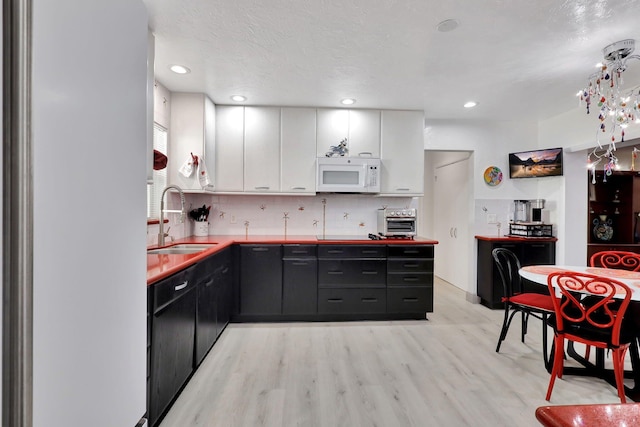 kitchen featuring sink, tasteful backsplash, a textured ceiling, light wood-type flooring, and white cabinets