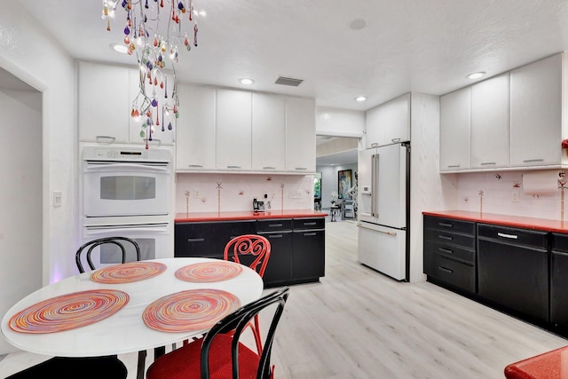 kitchen featuring white appliances, light wood-type flooring, decorative backsplash, and white cabinets