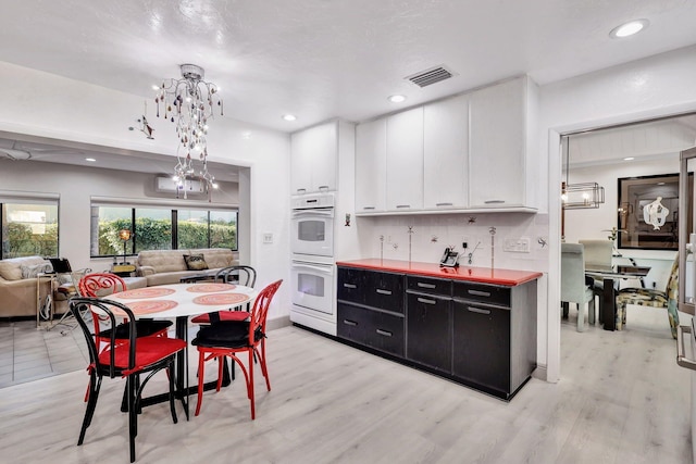 kitchen featuring hanging light fixtures, white cabinetry, white double oven, and light hardwood / wood-style flooring