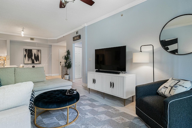 living room with ceiling fan, ornamental molding, light hardwood / wood-style flooring, and a textured ceiling