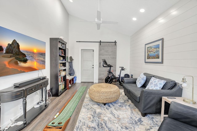 living room with lofted ceiling, hardwood / wood-style flooring, ceiling fan, a barn door, and wood walls