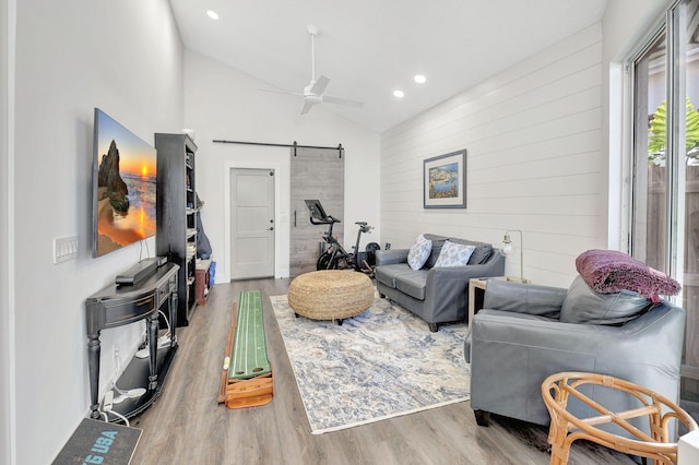 living room with lofted ceiling, wood walls, wood-type flooring, ceiling fan, and a barn door