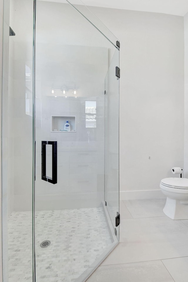 bathroom featuring toilet, a shower with shower door, and tile patterned flooring