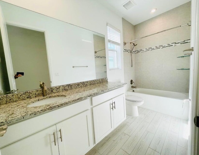 full bathroom with vanity, tiled shower / bath, hardwood / wood-style floors, and toilet