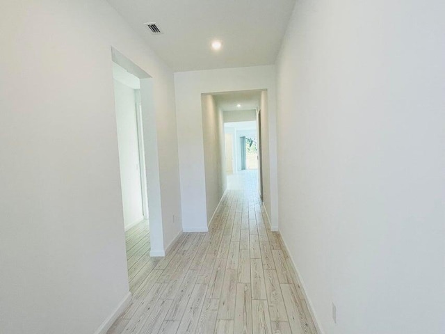 hall featuring baseboards, visible vents, and light wood finished floors