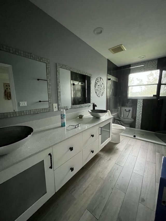 full bath featuring double vanity, toilet, a stall shower, wood tiled floor, and a sink