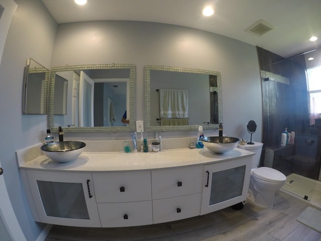 bathroom with a stall shower, visible vents, toilet, wood finished floors, and a sink