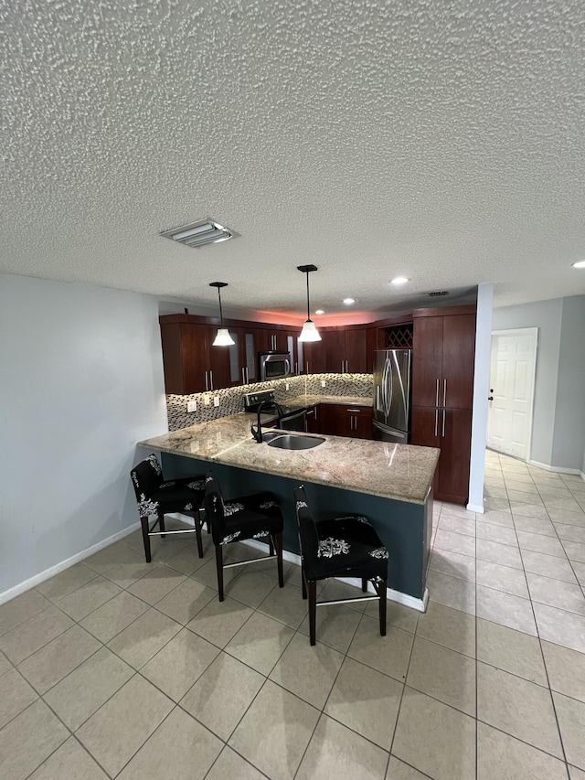 kitchen with light tile patterned flooring, a peninsula, a sink, appliances with stainless steel finishes, and backsplash