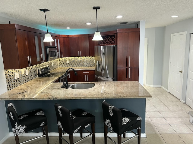 kitchen with light tile patterned flooring, stainless steel appliances, a peninsula, a sink, and pendant lighting