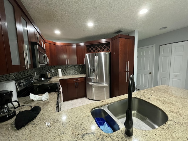 kitchen with light stone counters, stainless steel appliances, a sink, dark brown cabinets, and decorative backsplash