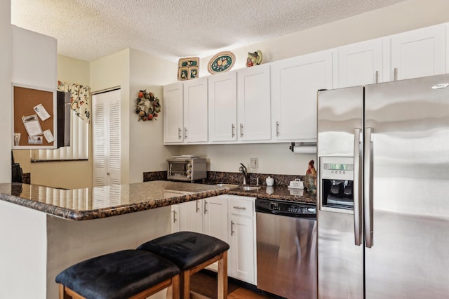 kitchen featuring stainless steel appliances, a breakfast bar, dark stone countertops, and white cabinets