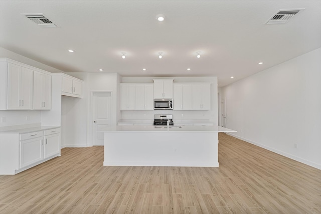 kitchen with white cabinetry, stainless steel appliances, a kitchen island with sink, and light hardwood / wood-style flooring