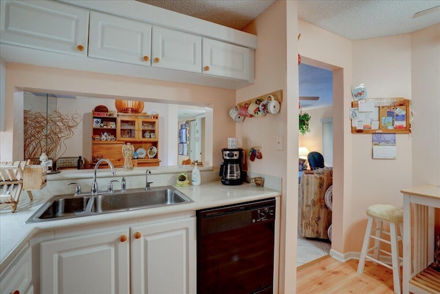 kitchen featuring white cabinetry, black dishwasher, sink, light wood-type flooring, and a textured ceiling