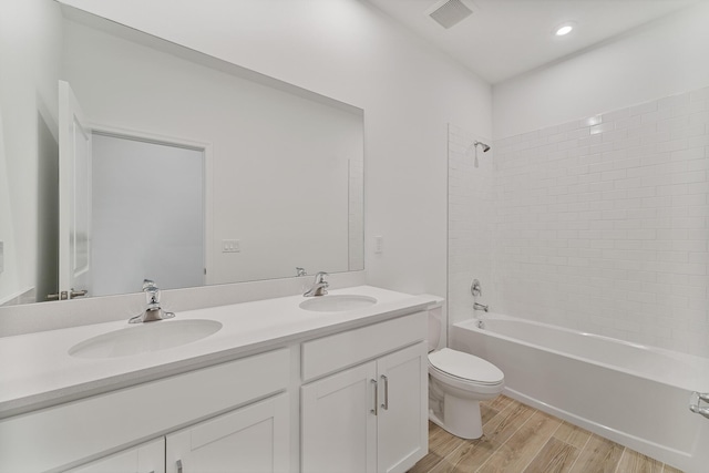 full bathroom featuring hardwood / wood-style flooring, tiled shower / bath, vanity, and toilet