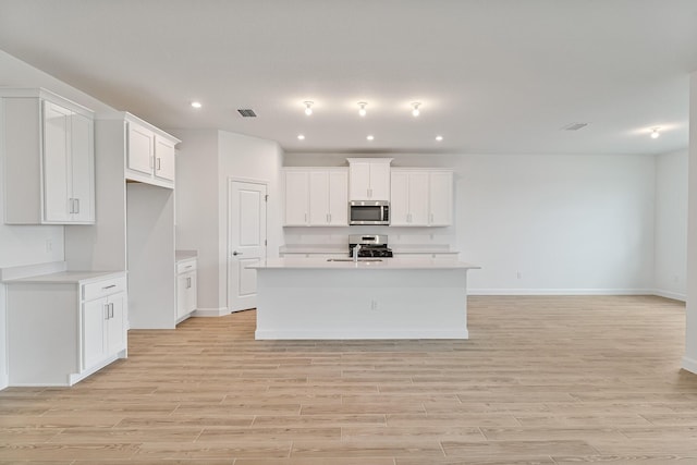 kitchen with stainless steel appliances, an island with sink, sink, and white cabinets