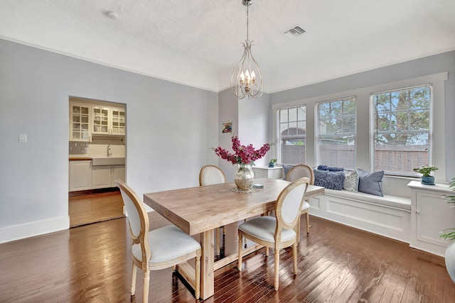 dining space featuring dark wood-type flooring, sink, a notable chandelier, and a textured ceiling