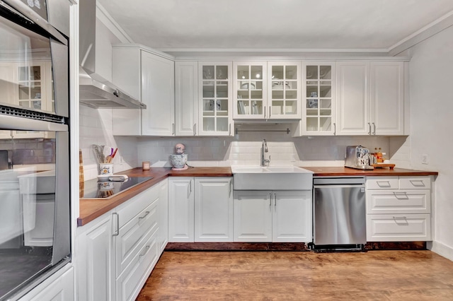 kitchen with sink, white cabinets, black electric stovetop, stainless steel oven, and wall chimney range hood