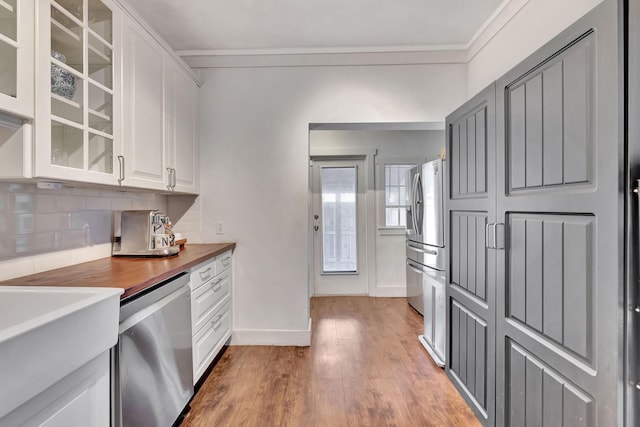 kitchen with appliances with stainless steel finishes, white cabinetry, hardwood / wood-style floors, butcher block counters, and decorative backsplash