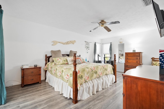 bedroom with a textured ceiling, light wood-style flooring, visible vents, baseboards, and a ceiling fan