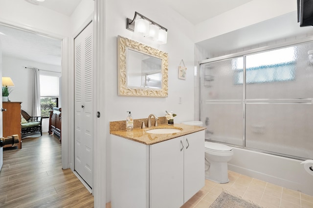 bathroom featuring toilet, combined bath / shower with glass door, a closet, and vanity