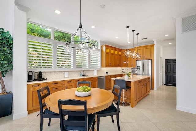 kitchen with light tile patterned floors, appliances with stainless steel finishes, light stone counters, a kitchen island, and decorative light fixtures