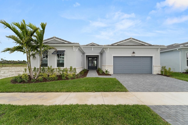 view of front of house featuring a garage, decorative driveway, a front lawn, and french doors