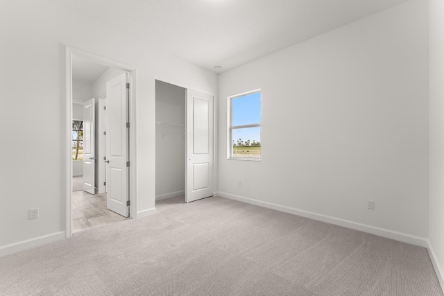 unfurnished bedroom featuring baseboards, light carpet, a closet, and ensuite bath