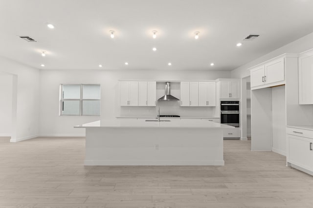 kitchen featuring a kitchen island with sink, white cabinets, wall chimney exhaust hood, and visible vents