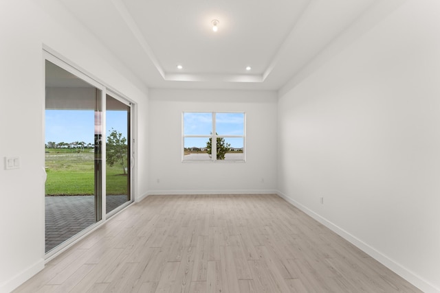 unfurnished room featuring recessed lighting, a tray ceiling, baseboards, and light wood-style flooring