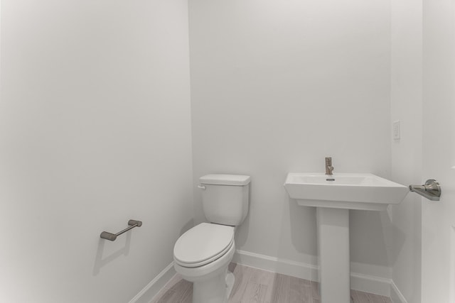 bathroom featuring wood finished floors, toilet, baseboards, and a sink