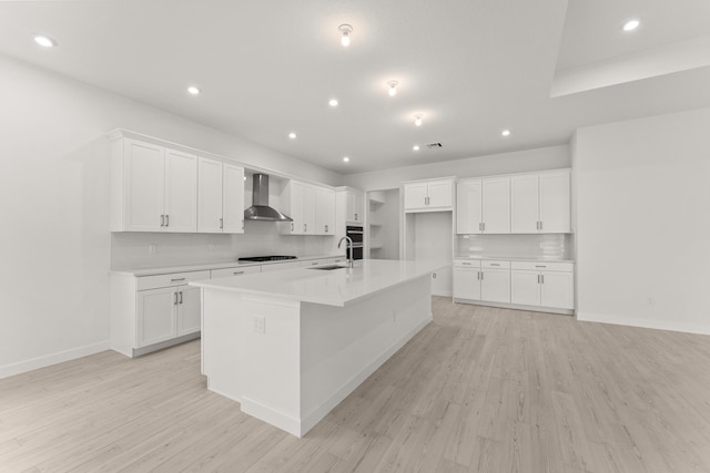 kitchen with a large island, a sink, light wood-style floors, wall chimney exhaust hood, and black cooktop