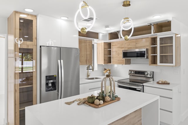 kitchen with sink, white cabinetry, decorative light fixtures, appliances with stainless steel finishes, and a kitchen island