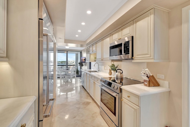 kitchen featuring recessed lighting, a sink, light countertops, appliances with stainless steel finishes, and cream cabinetry