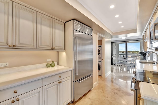 kitchen featuring recessed lighting, a sink, light countertops, stainless steel built in refrigerator, and stacked washer and clothes dryer