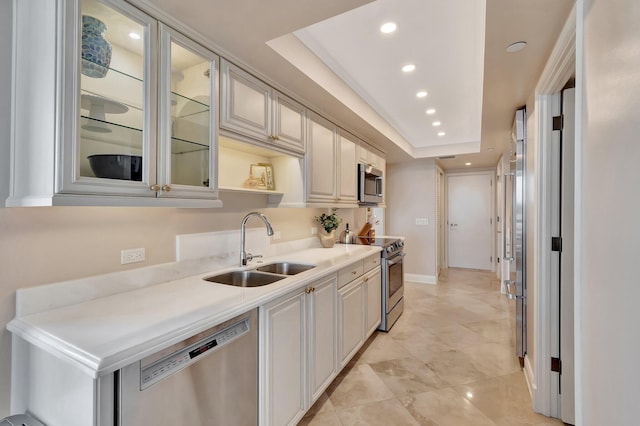 kitchen featuring a raised ceiling, appliances with stainless steel finishes, light countertops, a sink, and recessed lighting