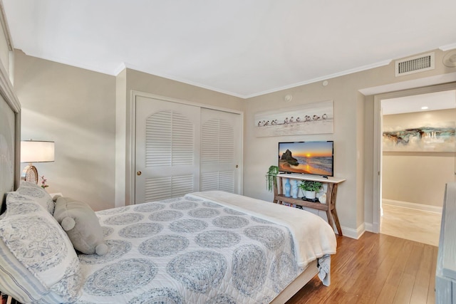 bedroom featuring a closet, wood finished floors, visible vents, and crown molding