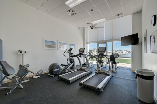 exercise room featuring ceiling fan, a high ceiling, a drop ceiling, and visible vents