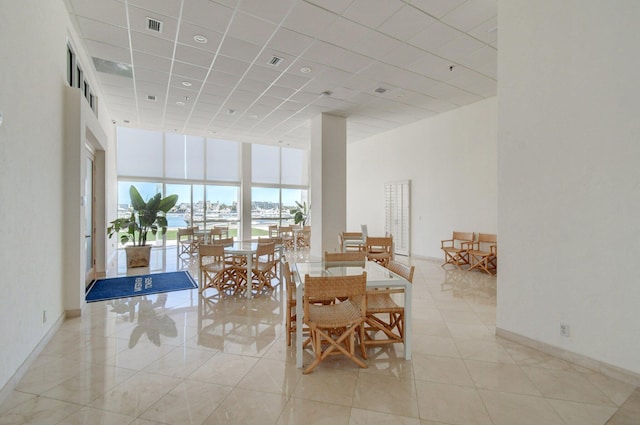 unfurnished dining area featuring visible vents, a towering ceiling, a drop ceiling, baseboards, and tile patterned floors