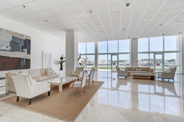 living area with visible vents, a towering ceiling, light tile patterned flooring, a wall of windows, and a drop ceiling