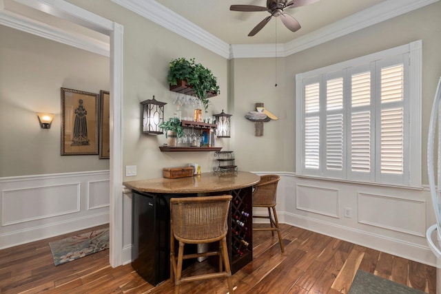 dining room featuring dark wood-type flooring, ceiling fan, bar area, and crown molding