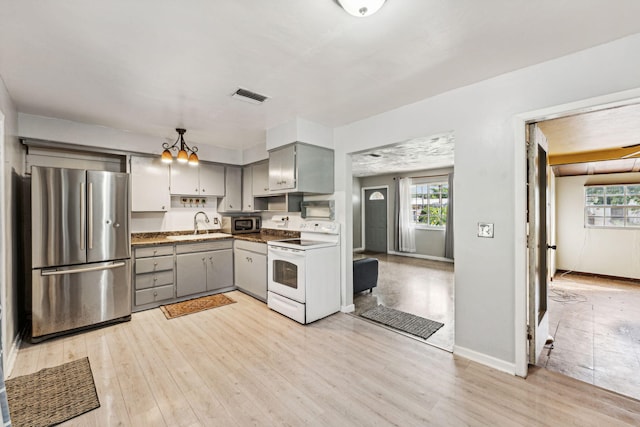 kitchen with gray cabinets, appliances with stainless steel finishes, decorative light fixtures, sink, and light hardwood / wood-style floors