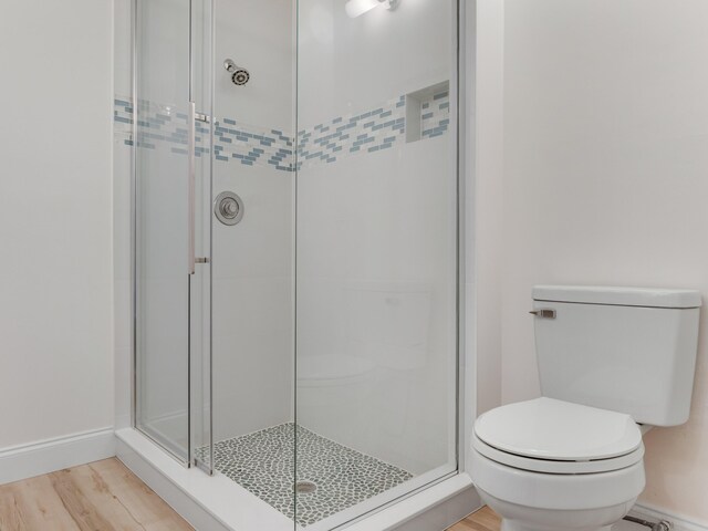 bathroom with wood-type flooring, a shower with door, and toilet