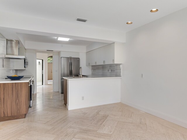 kitchen featuring stainless steel refrigerator, white cabinetry, sink, light parquet flooring, and wall chimney exhaust hood