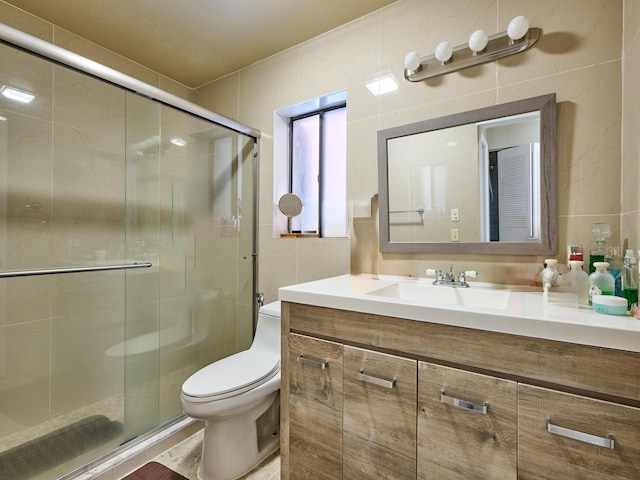 bathroom featuring vanity, toilet, a shower with door, and tile walls