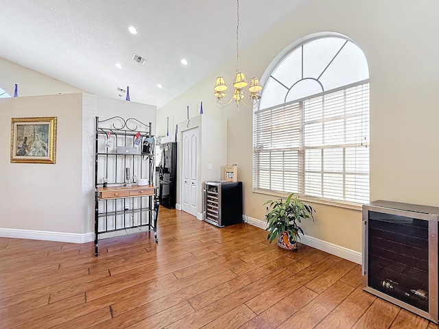 interior space featuring high vaulted ceiling, wine cooler, a notable chandelier, a textured ceiling, and light hardwood / wood-style flooring