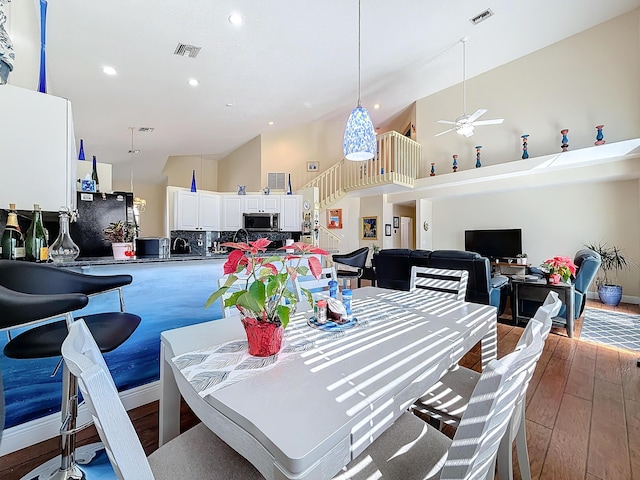 dining room with hardwood / wood-style flooring, high vaulted ceiling, and ceiling fan