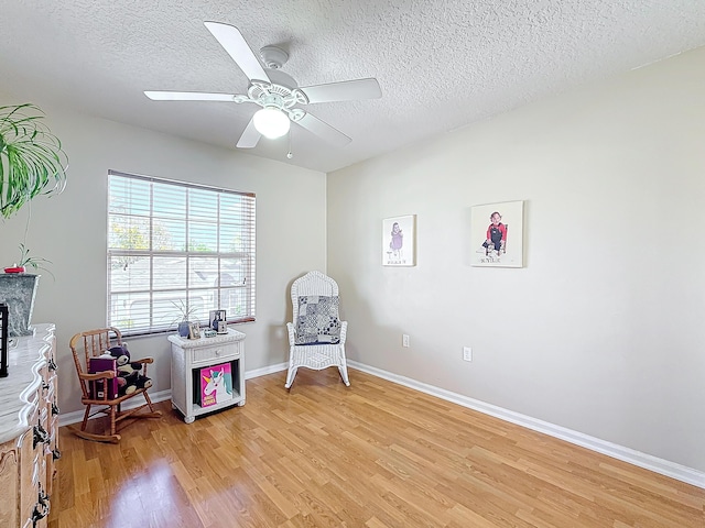 living area with ceiling fan, a textured ceiling, and light hardwood / wood-style floors