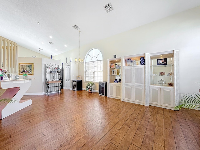 unfurnished living room with hardwood / wood-style floors, vaulted ceiling, beverage cooler, and a chandelier