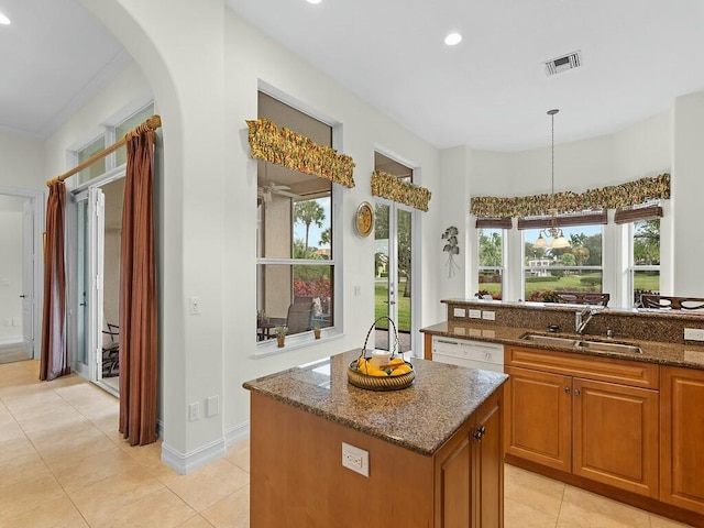 kitchen featuring sink, white dishwasher, a kitchen island, decorative light fixtures, and dark stone counters